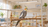 Cockatiel on a natural wood perch with an overhead lighting fixture outside the cage