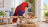 Female Eclectus parrot on a natural wood perch beside a bowl of vegetables